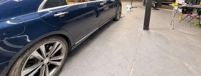Dark sedan side panel with visible scratches at the M&A workshop