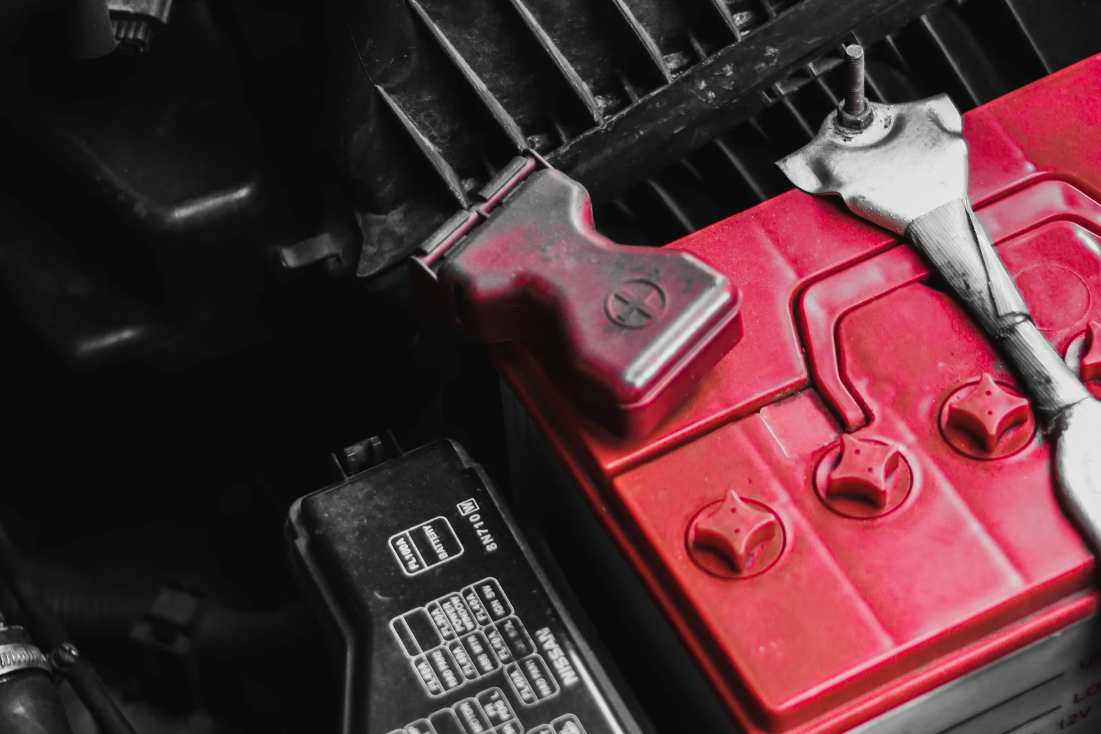 Red car battery and terminal connections inside an engine bay.