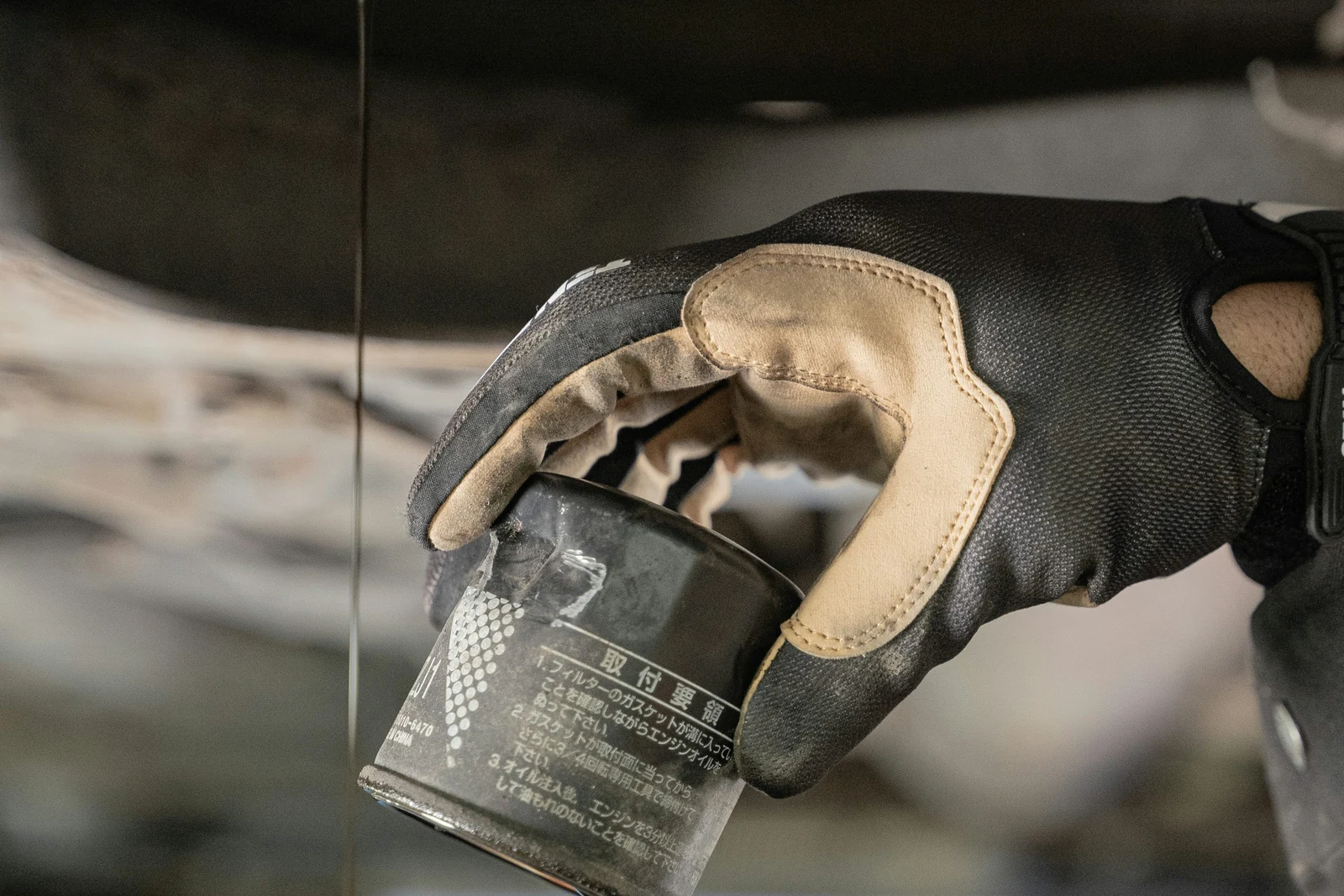 Gloved hand holding an oil filter beneath a vehicle as oil drains.