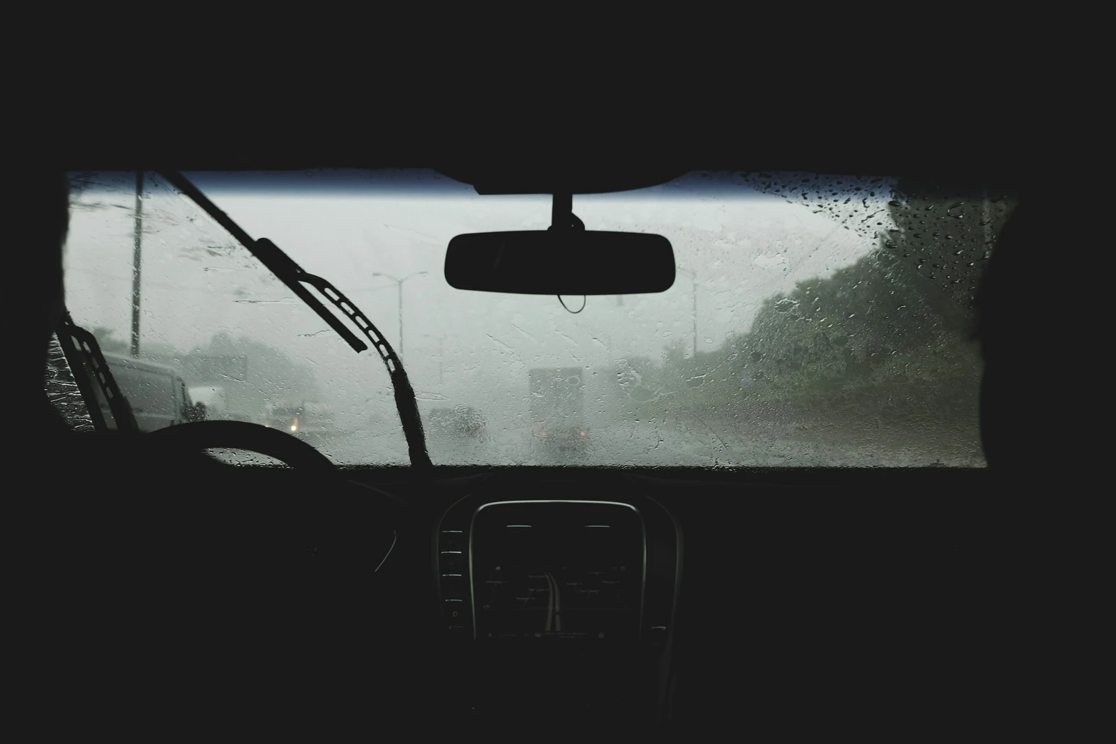 Rainy road seen through a windshield with the wipers in motion.